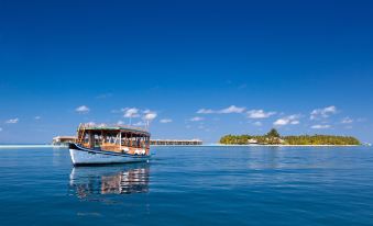 a small boat sailing on a calm blue sea , with the ocean visible in the background at Vilamendhoo Island Resort & Spa