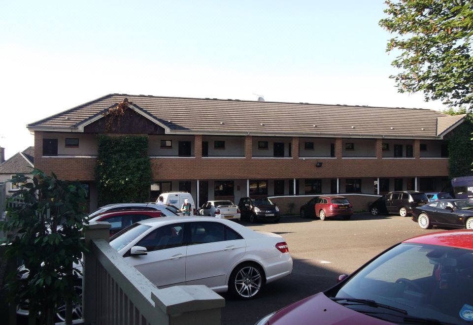 a parking lot with numerous cars parked , some of which are white in color , and a building with a brown roof at Richmond Park Hotel