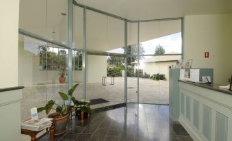 a modern , glass - enclosed lobby with large windows and sliding doors , featuring a reception area and potted plants at The Aston Motel Tamworth