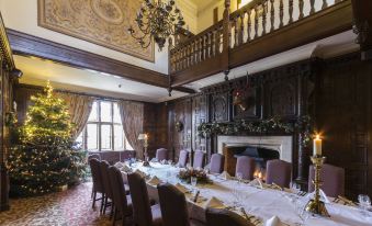 a large dining room with a long table set for a formal dinner , surrounded by chairs and decorated for the holiday season at The Billesley Manor Hotel