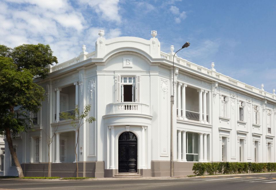 a white , ornate building with black shutters and an arched entrance is shown on a street at Hotel B