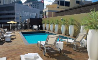 a rooftop deck with a swimming pool surrounded by lounge chairs and potted plants , providing a relaxing outdoor space at Vibe Hotel Sydney