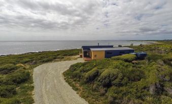 a house with a yellow exterior and blue roof is situated on a sandy beach near the ocean at Seaspray
