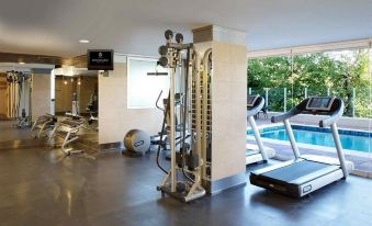 a gym with various exercise equipment and a swimming pool in the background , under a white ceiling at DiplomaticHotel