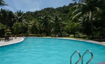 a large swimming pool surrounded by palm trees , with people enjoying their time in the water at Perhentian Island Resort