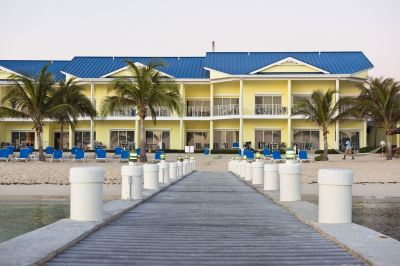 a beach resort with a yellow building and blue umbrellas on the sandy shore , along with a walkway leading to the water at Wyndham Reef Resort Grand Cayman