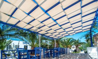 an outdoor dining area under a large blue and white striped tent , surrounded by palm trees at Syros Atlantis