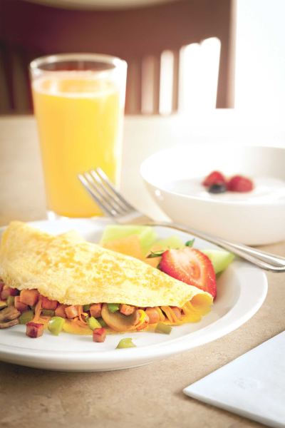 a breakfast plate with a sandwich , fruit salad , and a cup of orange juice on a table at Country Inn & Suites by Radisson, Watertown, SD