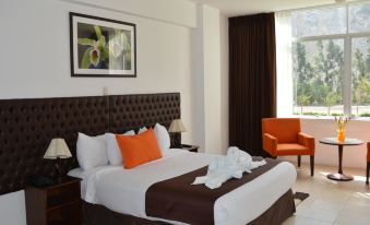 a large bed with a brown headboard and white linens is in a room with an orange chair at Guizado Portillo Hacienda & Resort