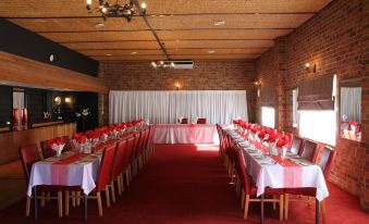 a large dining room with red tables and chairs , white tablecloths , and a brick wall at Golden Age Motor Inn