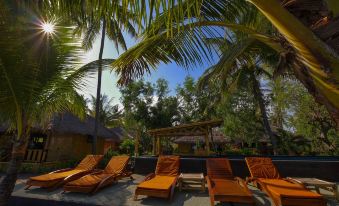 a tropical resort with multiple lounge chairs arranged in a row , surrounded by palm trees and a blue sky at Rinjani Beach Eco Resort