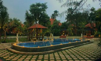 a large outdoor swimming pool surrounded by lush greenery , with a gazebo in the background at Ubud Hotel & Cottages