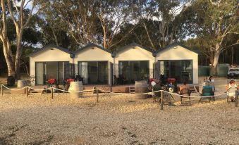 a group of three small white cabins , each with a bench and table , surrounded by trees and gravel at Coonawarra Bush Holiday Park