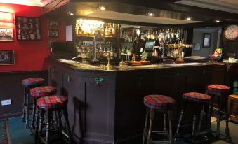 a bar with several stools and a long counter filled with bottles and glasses , surrounded by red walls at Cross Keys