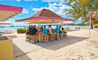 a group of people gathered around a wooden table on a sandy beach , enjoying a meal and socializing at Anegada Reef Hotel