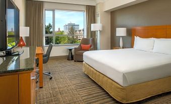 a hotel room with a large bed , desk , and chair , as well as a view of the city outside the window at Hilton Vancouver Washington