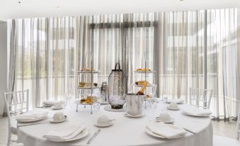 a dining table set with white plates , silverware , and wine glasses , surrounded by a striped tablecloth and a window with curtains at Sage Hotel Wollongong