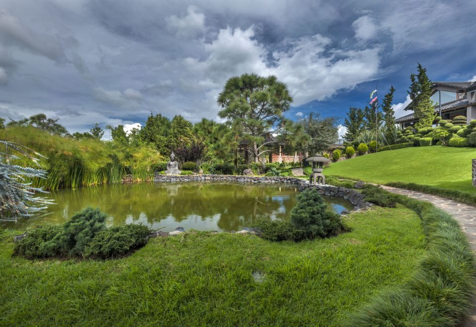 a serene garden with a pond , trees , and people walking on a path under a cloudy sky at Koanze Luxury Hotel & Spa