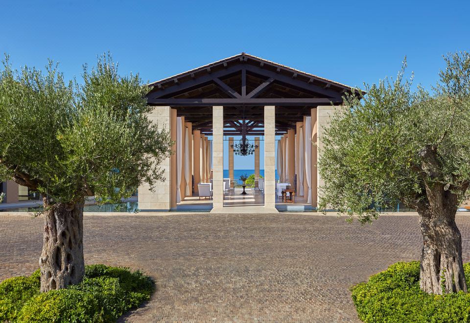 a large wooden gazebo situated near a body of water , with chairs and tables set up for outdoor dining at The Romanos, a Luxury Collection Resort, Costa Navarino