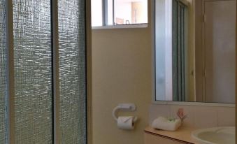 a bathroom with a toilet , sink , and mirror , as well as a window with glass panes at The Mullum Motel