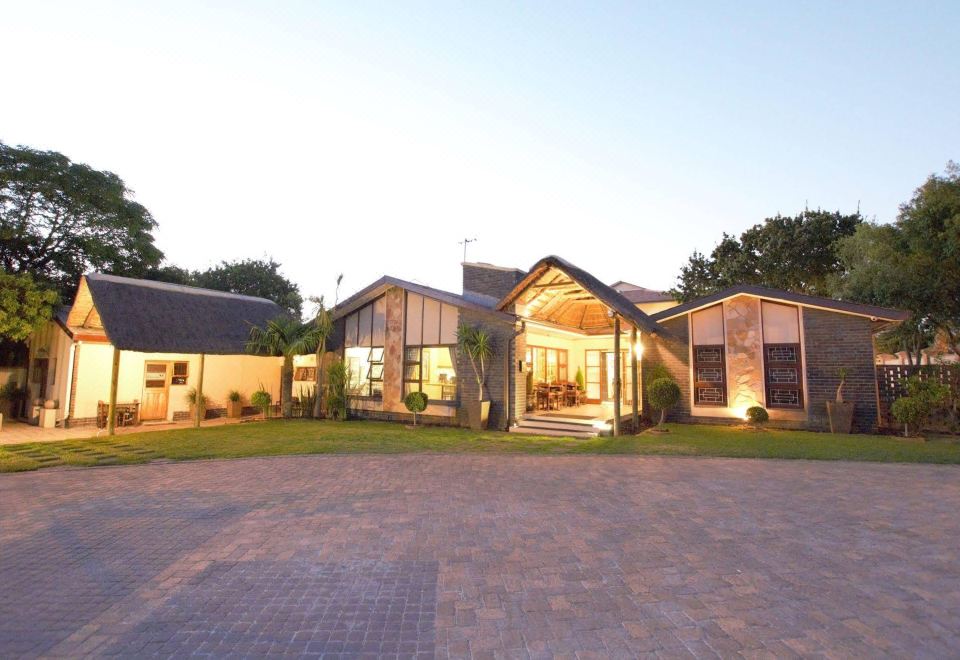 a large house with a patio and brick driveway , surrounded by trees and grass , at dusk at Balmoral Lodge