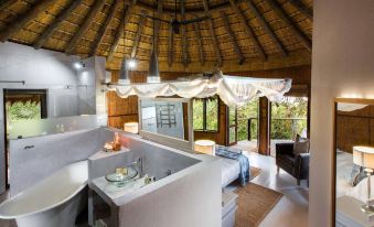 a luxurious bathroom with a bathtub , shower , and bathtub accessories under a thatched roof at Thonga Beach Lodge