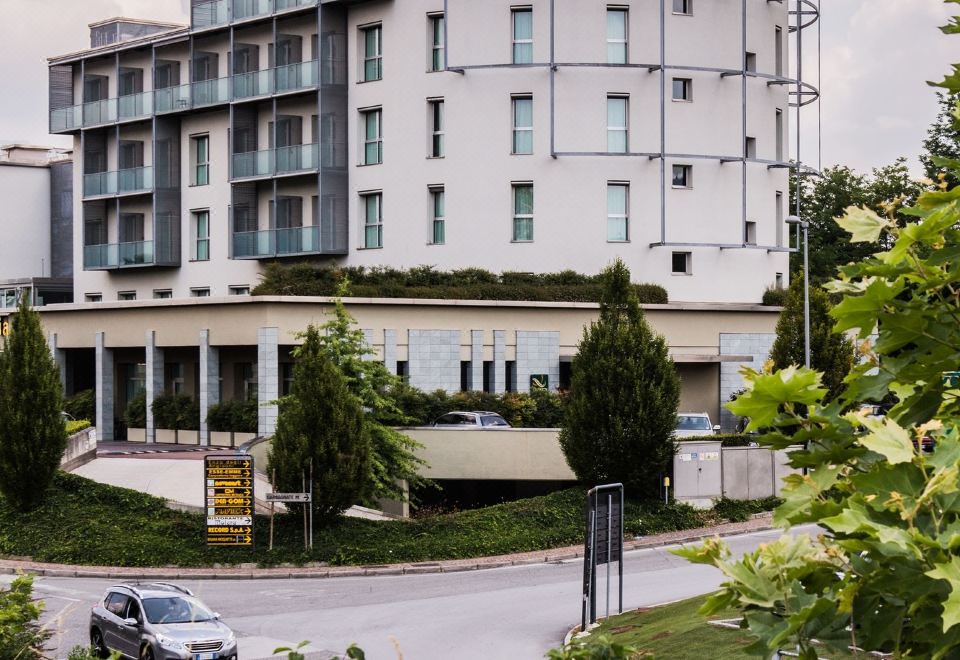 "a large white building with a sign that reads "" hotel san martino "" is surrounded by trees and a road" at Quality Hotel San Martino
