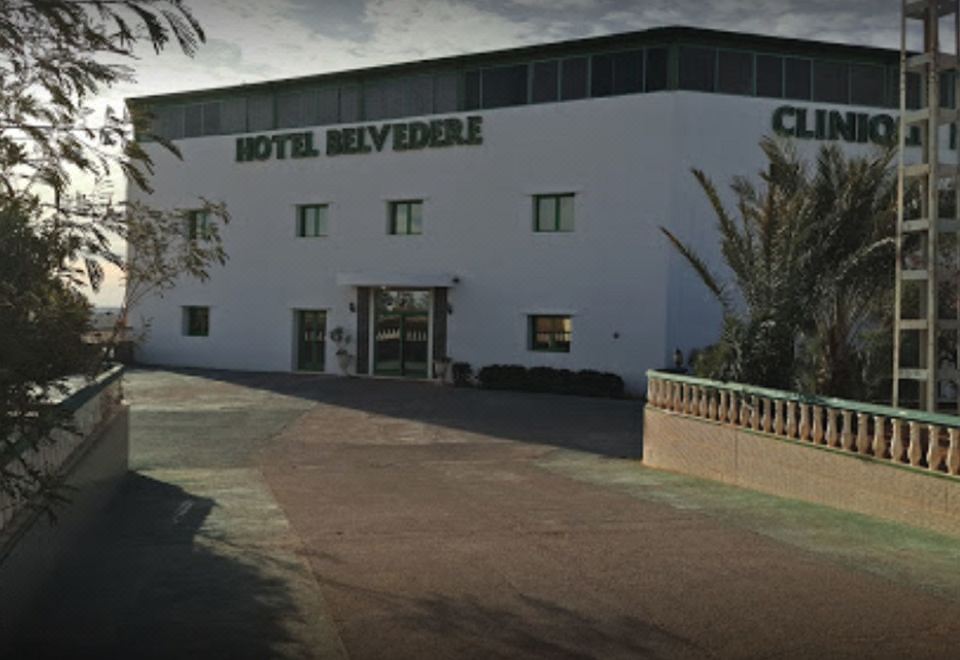 "a large white building with the words "" hotel belvedere "" written on it , surrounded by trees and a driveway" at Hotel Belveder