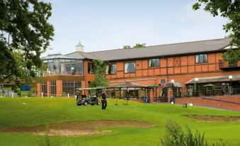a large brick building surrounded by a golf course , with a group of people playing golf in the background at Macdonald Hill Valley Hotel, Golf and Spa