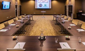a conference room with several tables and chairs , a screen displaying a pie chart , and a clock on the wall at Holiday Inn Owensboro Riverfront