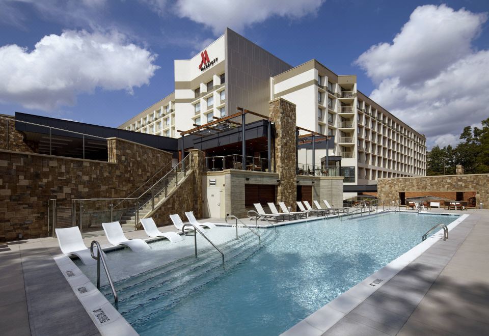 a large swimming pool with a hotel in the background and white lounge chairs around it at Raleigh Marriott Crabtree Valley