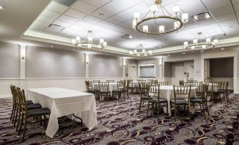 a large , empty conference room with multiple rows of tables and chairs , chandeliers hanging from the ceiling , and a podium in the center at Park Manor Hotel