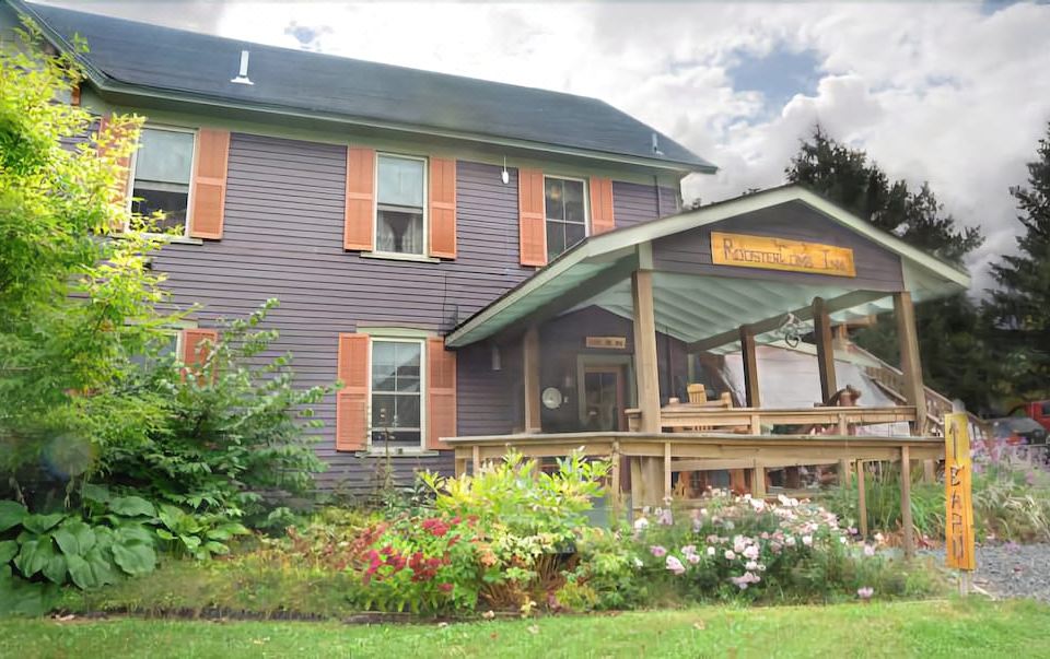 a house with a purple roof and orange shutters is surrounded by greenery and flowers at RoosterComb Inn