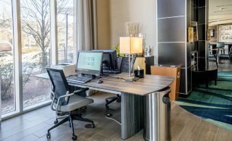 a modern office setup with a desk , chairs , and a computer monitor , all set up in front of large windows at SpringHill Suites Pueblo Downtown