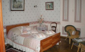 a cozy bedroom with wooden furniture , including a bed , dresser , and chair , surrounded by white walls decorated with floral wallpaper at Le Chateau