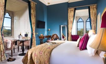 a luxurious hotel room with a large bed , blue walls , and gold accents , including a chandelier and a desk at Kilkea Castle