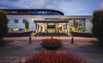 a modern building with a large glass facade is surrounded by red flowers and set in a well - maintained courtyard at Van der Valk Hotel Middelburg