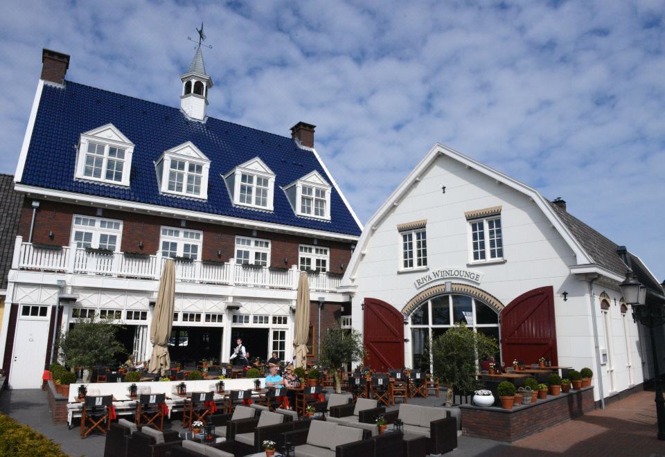 a large white building with a blue roof and two red - tiled turrets is next to an outdoor patio area at Fletcher Hotel - Restaurant Nautisch Kwartier