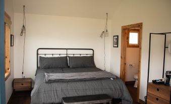 a bedroom with a large bed and gray bedding , a bench in the corner , and a door leading to another room at Big Arm Resort