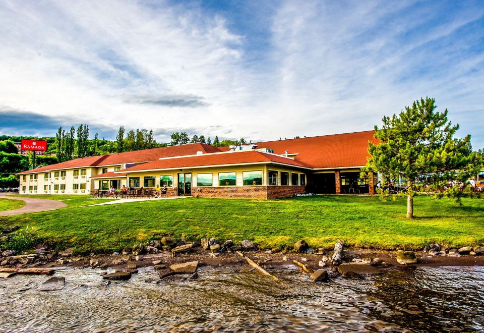 a large building with a red roof is surrounded by grass and trees near a river at Ramada by Wyndham Hancock Waterfront