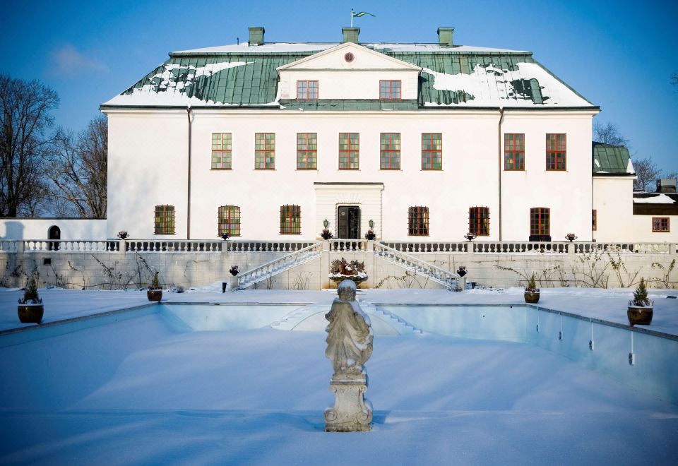 a large white building with green roof and snow on the ground , surrounded by snow - covered sculptures at Haringe Slott