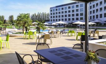 an outdoor dining area with several tables and chairs , surrounded by a swimming pool and a building at Ibis Styles Milano Est Settala