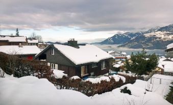 a snow - covered house with a green roof is nestled in the foreground , while mountains and buildings can be seen in the background at Annex