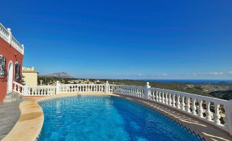 a large outdoor swimming pool surrounded by a white fence , with a view of the ocean in the background at Esperanza