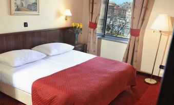 a well - lit hotel room with a red bed , white pillows , and a view of the city through the window at Hotel Continental