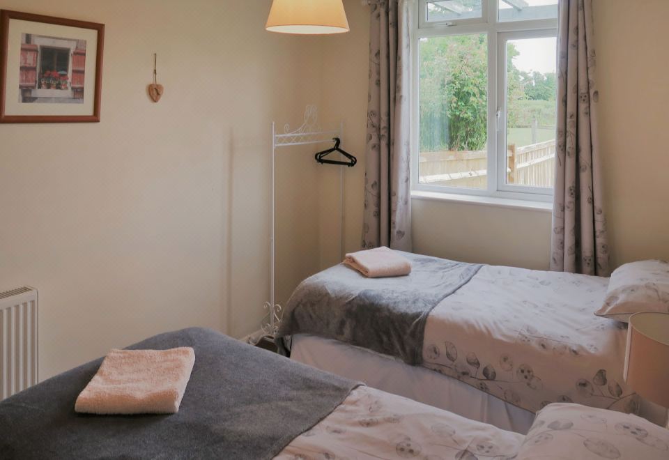 a bedroom with two beds , a window , and a coat rack , decorated with towels on the beds at Woodhouse Woodmancote