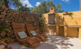 a patio area with wooden chairs and a stone wall , surrounded by trees and a fireplace at Villa Mare