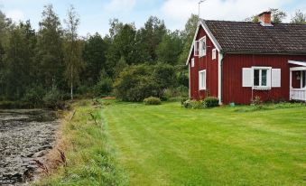 a red house surrounded by green grass and trees , with a body of water in the background at Vadstena