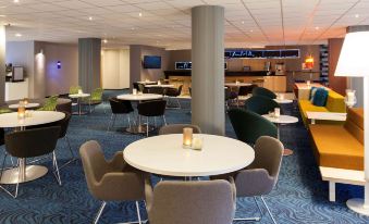 a modern lounge area with blue and white carpet , tables , chairs , and a bar at Novotel Maastricht