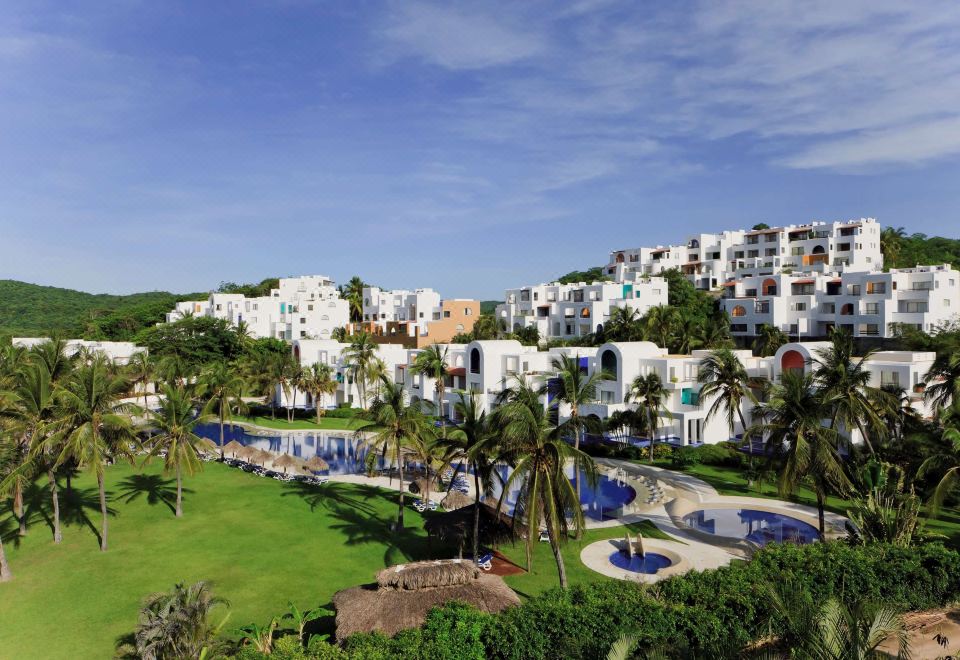 a tropical resort with white buildings , lush greenery , and a clear blue pool surrounded by palm trees at Camino Real Zaashila Huatulco